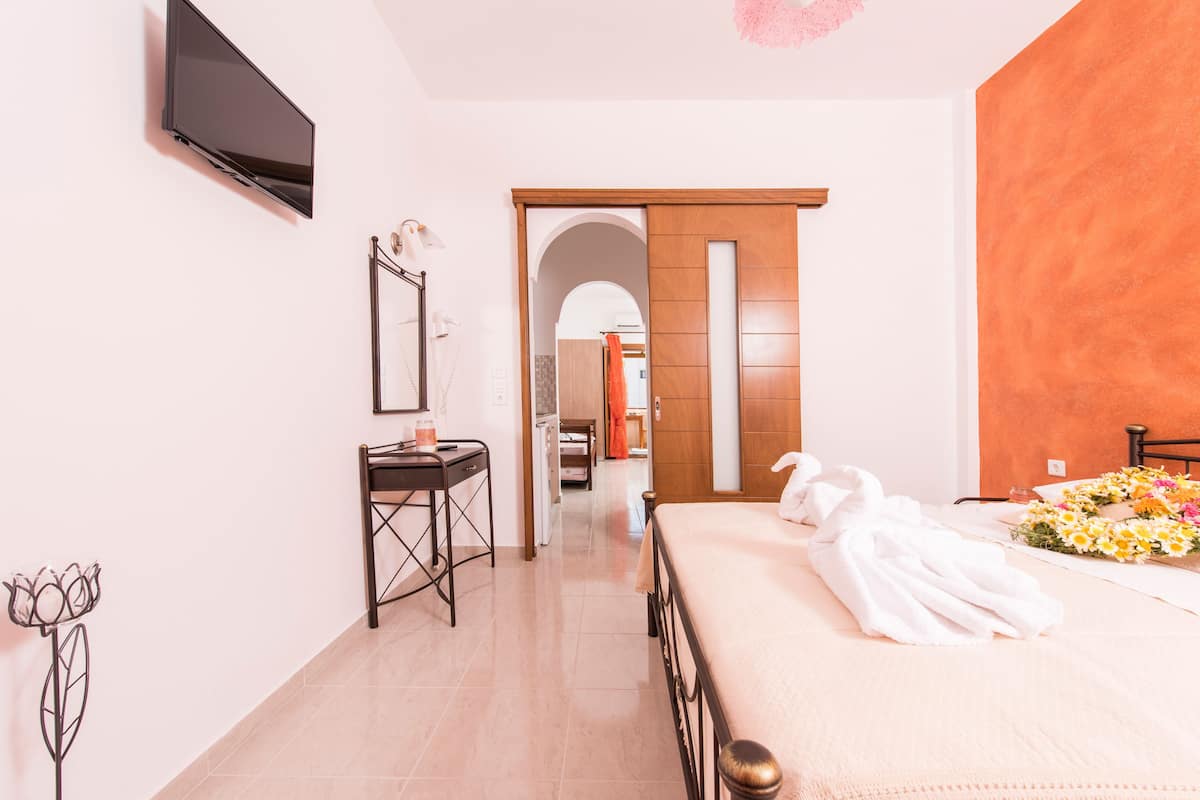 A hotel room with a bed, a desk, a TV, and a bathroom visible through an archway.