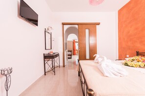 A hotel room with a bed, a desk, a TV, and a bathroom visible through an archway.