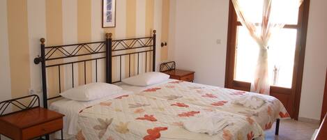A bedroom with a bed, two bedside tables, a nightstand, a window with curtains, and a wall-mounted air conditioner.