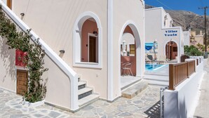 A building with a stone-paved entrance, a wooden staircase, and a sign reading "Villas Vouli". - Villa Voula (Santorini)