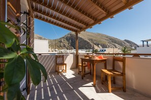 A wooden balcony with a table and chairs, overlooking a mountainous landscape.