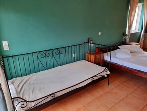 A room with a single bed with a metal frame and a white mattress, a wooden nightstand with a lamp, and a window with curtains. - O Xenonas ton Mylon (Argos-Mykines)