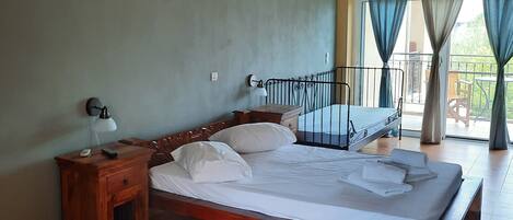 Quarto com cama de madeira, mesa de cabeceira, abajur e vista do exterior através de uma varanda.
