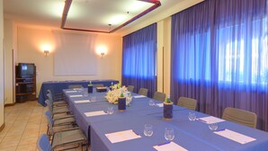 Un salón de conferencias con una larga mesa, sillas, una pantalla de proyector y cortinas.