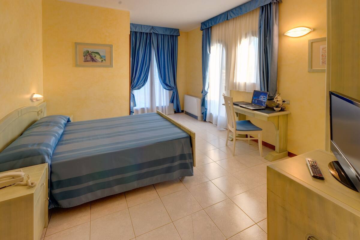 Habitación de hotel con cama, escritorio, silla, televisor y teléfono.