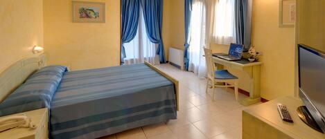 Habitación de hotel con cama, escritorio, silla, televisor y teléfono.