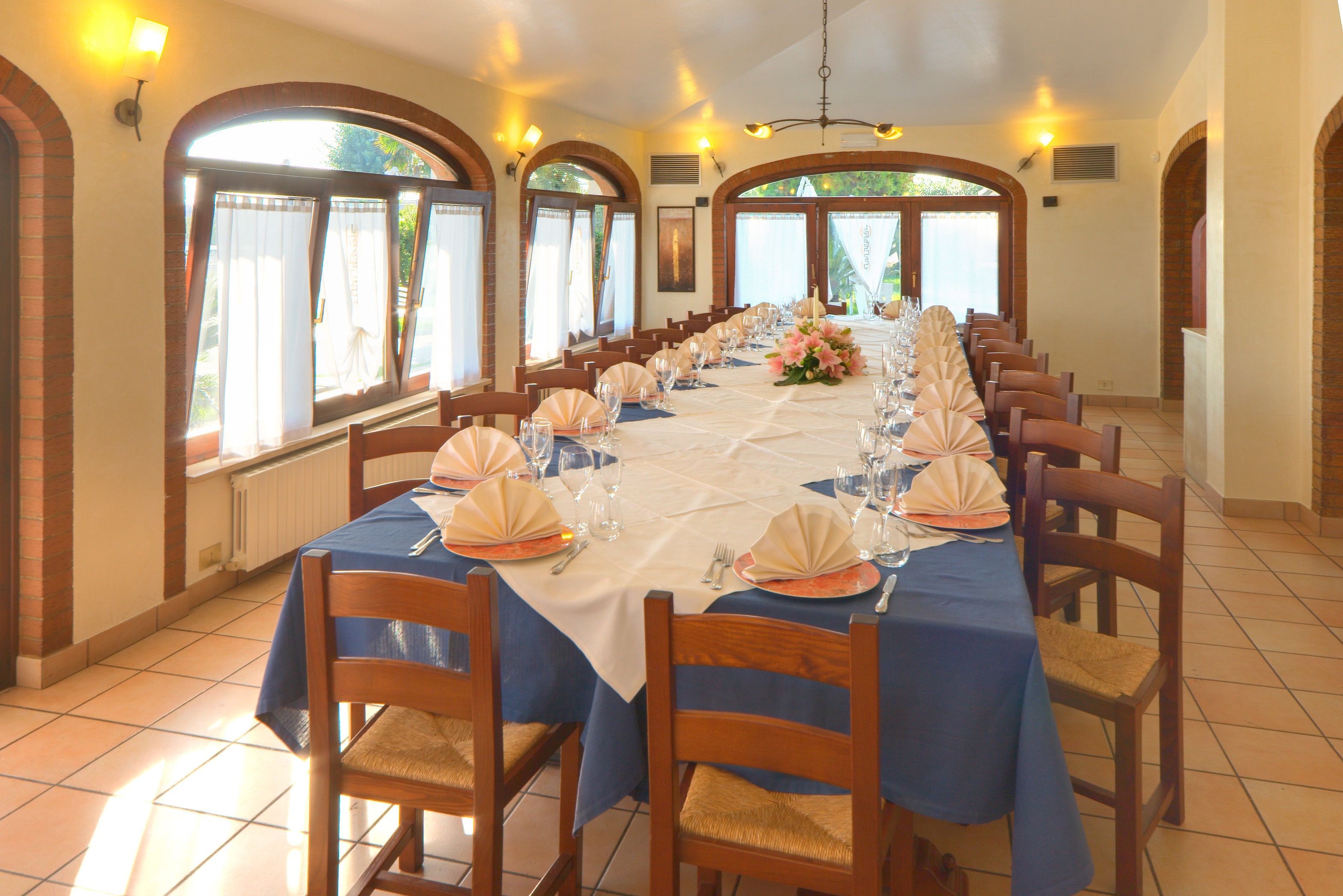 Un lungo tavolo imbandito per un evento formale, con sedie, tovaglie e composizioni floreali.