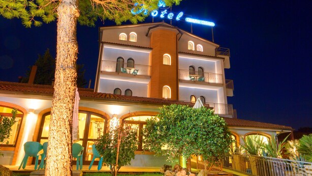 Un hotel con fachada bien iluminada, zona de estar al aire libre y un gran árbol en su parte frontal.