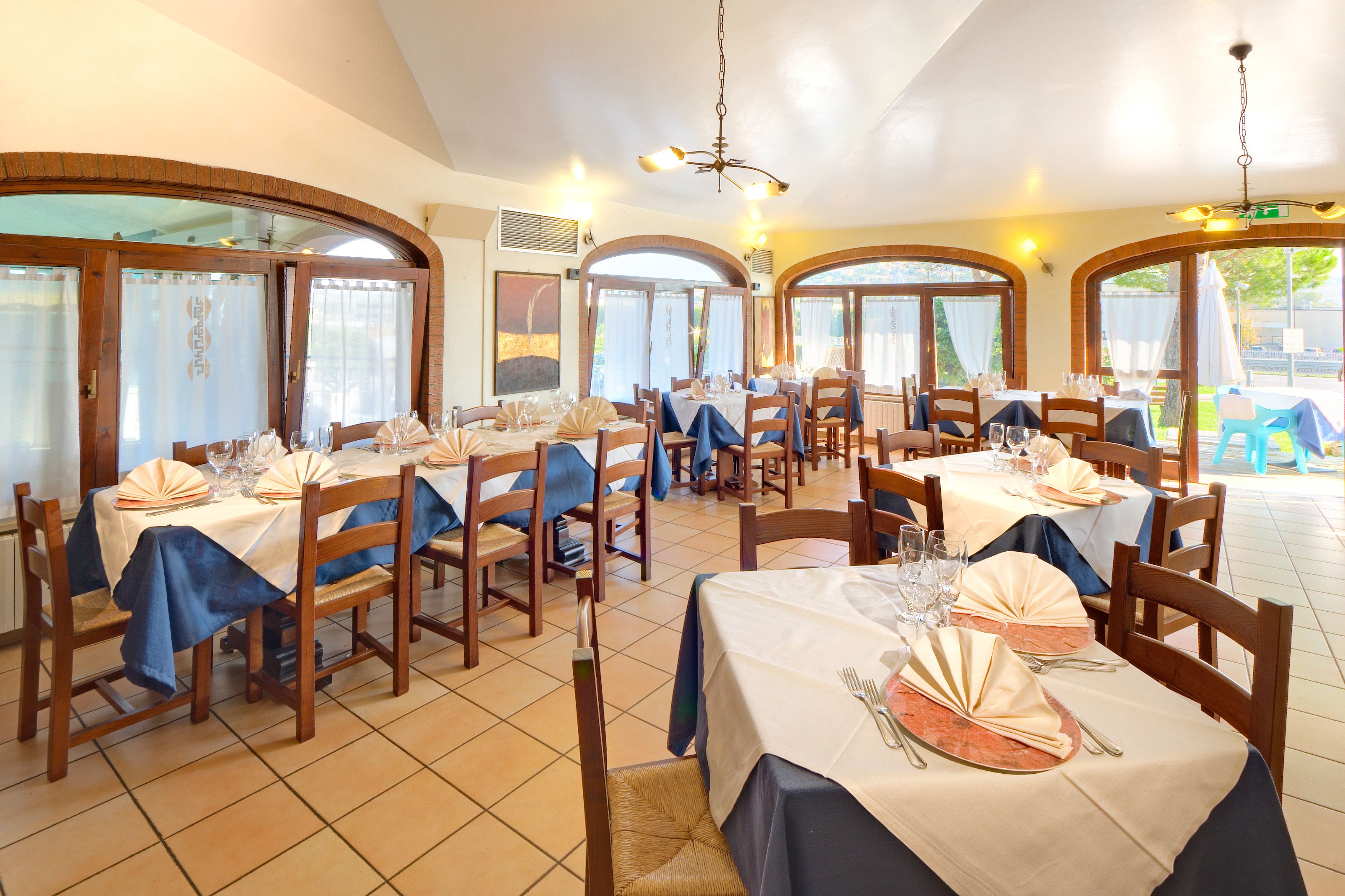 Een restaurant met meerdere tafels gedekt voor het dineren, met houten stoelen en tafels bekleed met witte tafellakens.