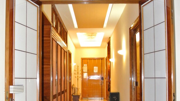 A hallway with a checkered floor, wooden doors, and a reception desk in the distance. - L'Aura di Sicilia (Ragusa)