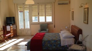A bedroom with a bed, a chair, a television, and a window with blinds. - L'Aura di Sicilia (Ragusa)