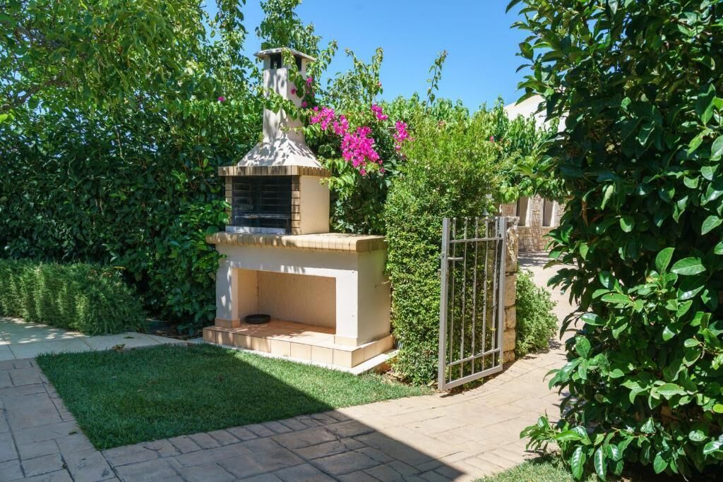A garden with a brick barbecue area, surrounded by greenery and a metal gate.