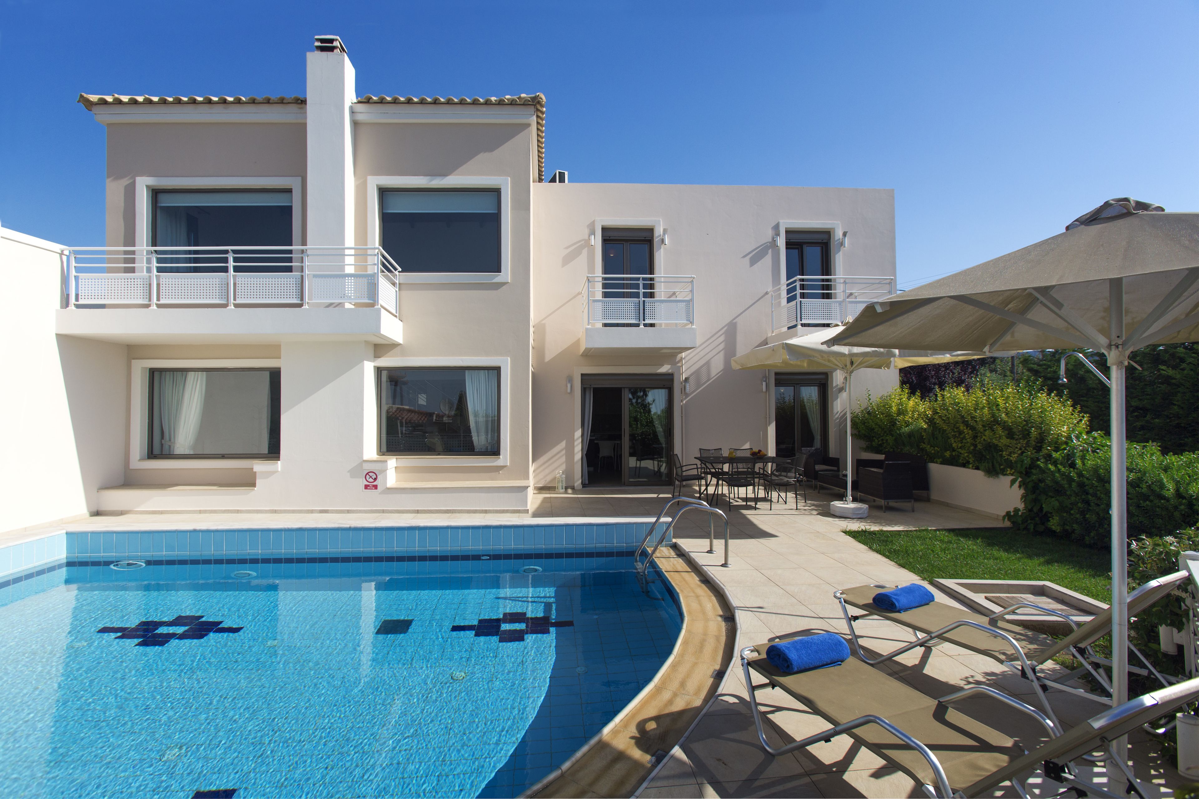 A modern two-story building with a swimming pool, outdoor seating, and a covered patio area.