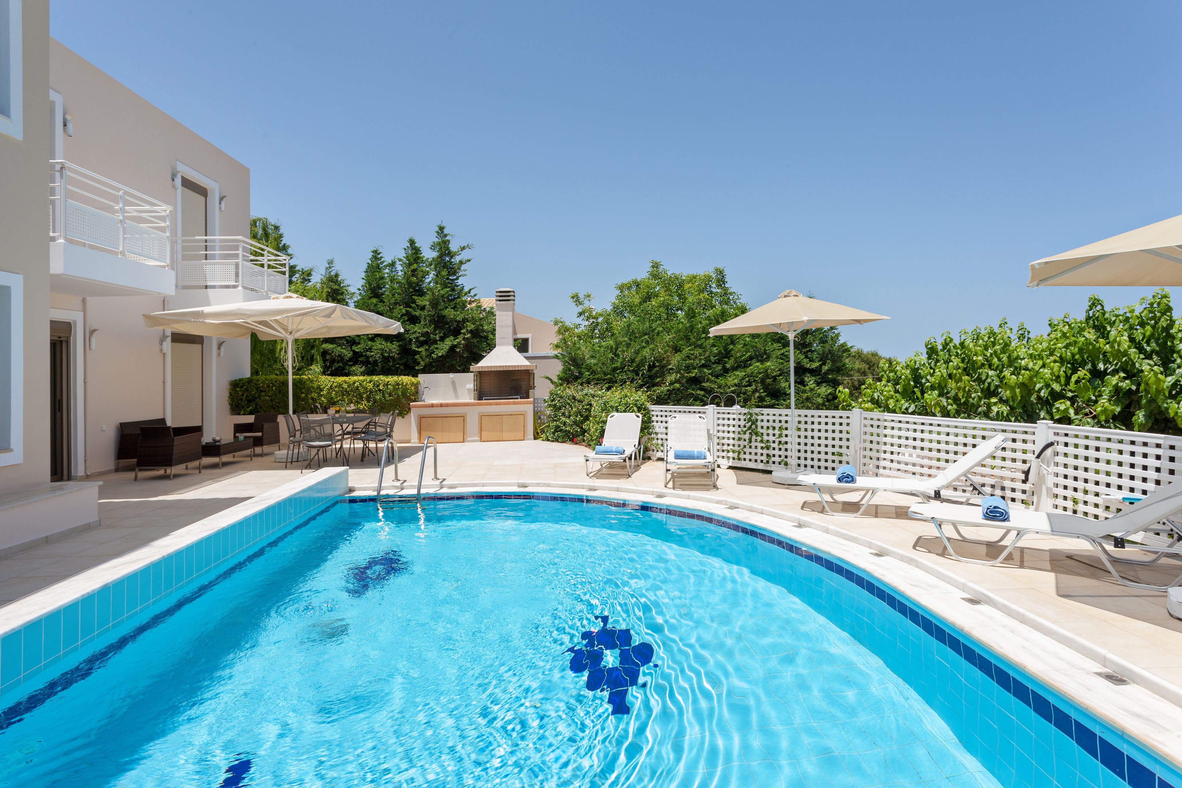 Una piscina amb aigua turquesa cristal·lina, envoltada de gandules i ombrelles, i un edifici amb balcó.