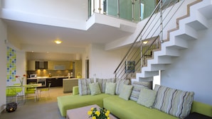 Sala de estar moderna com um sofá verde, uma mesa de centro com flores e uma escada que leva a um andar superior.