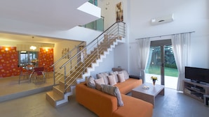 Uma sala moderna com escada, sofá, televisão e área de jantar.