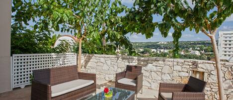 Un espace extérieur aménagé avec des meubles en osier et une table en verre, entouré de murs en pierre et de verdure.