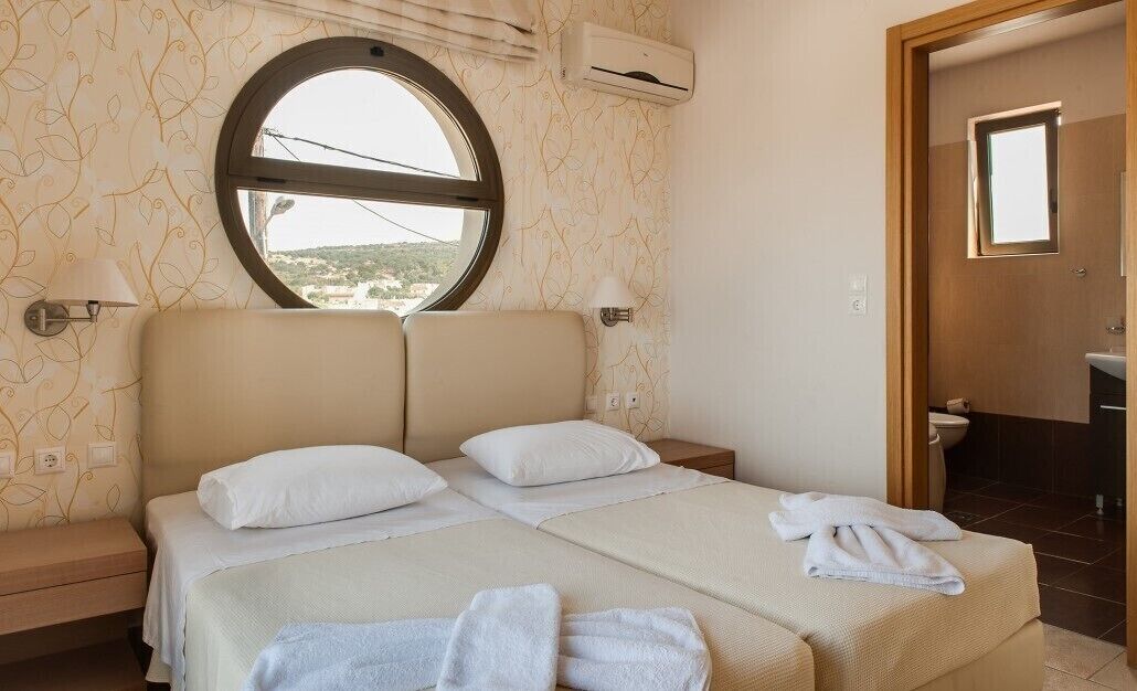 A bedroom with a large bed, two bedside tables, a round window, and a view of the outside.