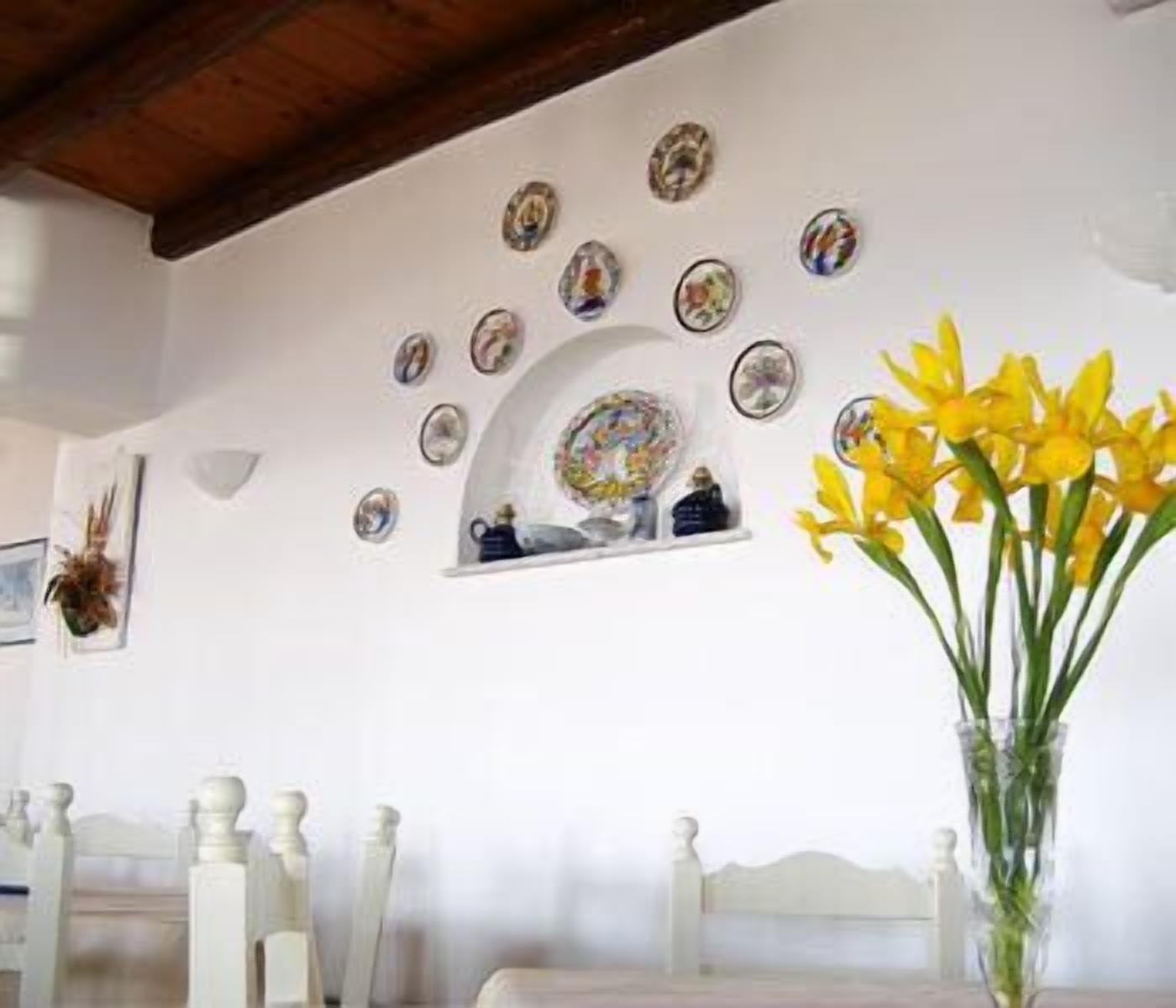 Una habitación con pared blanca decorada con detalles circulares, una mesa blanca con sillas y un jarrón con flores amarillas.