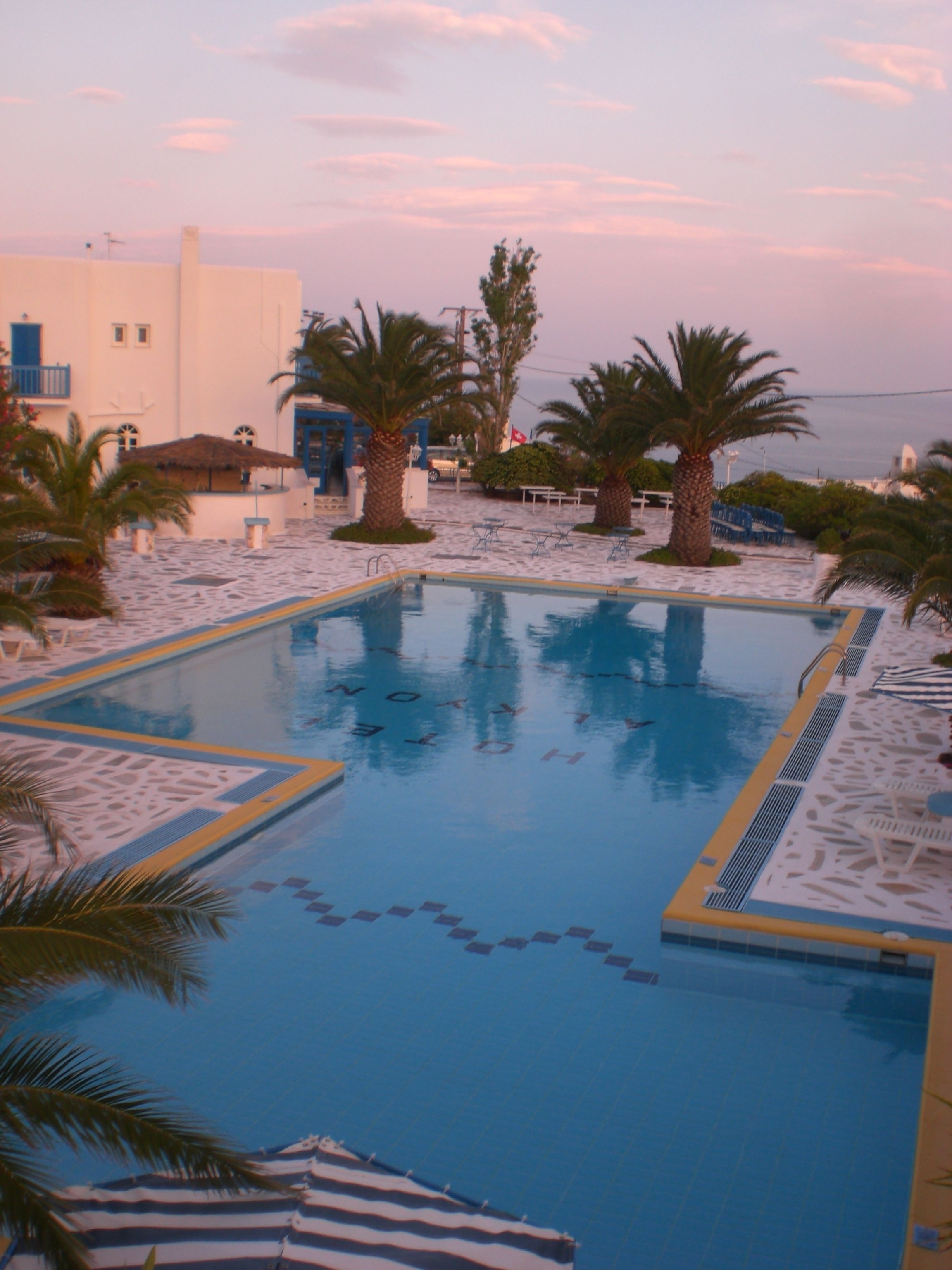 Una piscina con solárium empedrado, palmeras y un edificio al fondo.