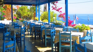 An outdoor café with blue furniture and yellow checkered tablecloths, overlooking a scenic view of the sea. - Hotel Alkyon (Syros)