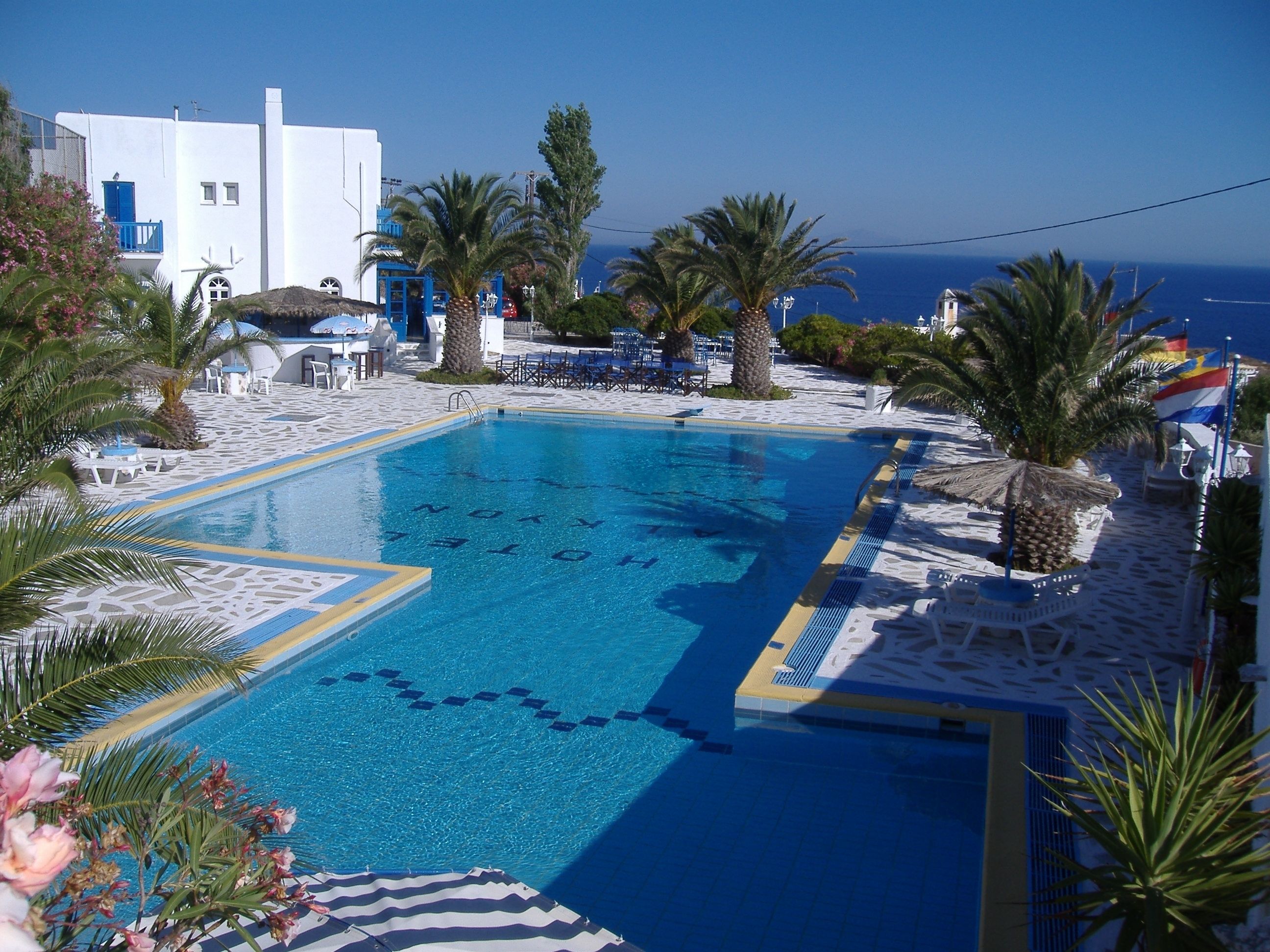A pool with clear blue water, surrounded by white buildings and palm trees.