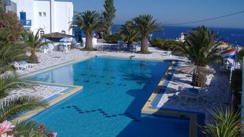 A pool with clear blue water, surrounded by white buildings and palm trees.