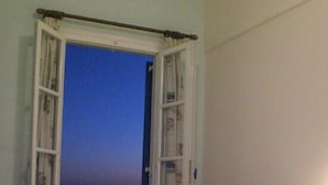 A hotel room with a bed, a nightstand, and a window with curtains. - Hotel Alkyon (Syros)
