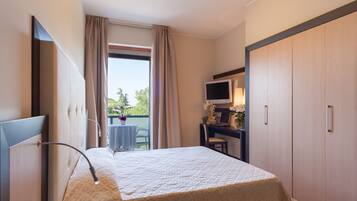 A hotel room with a bed, a desk with a computer, a TV, and a view of the outdoors.