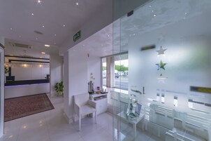 Een moderne hotellobby met een receptiebalie, een zithoek en een glazen wand met decoratieve elementen.