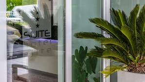 A hotel entrance with a glass door, a potted plant, and a sign indicating a 'Suite'. - Suite Hotel Elite (Bologna)