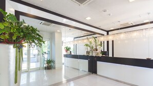 A modern hotel lobby with a reception desk, glass doors, and potted plants. - Suite Hotel Elite (Bologna)