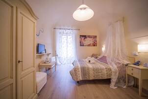 Un dormitorio con cama, mesita de noche, lámpara y televisión sobre una estantería.