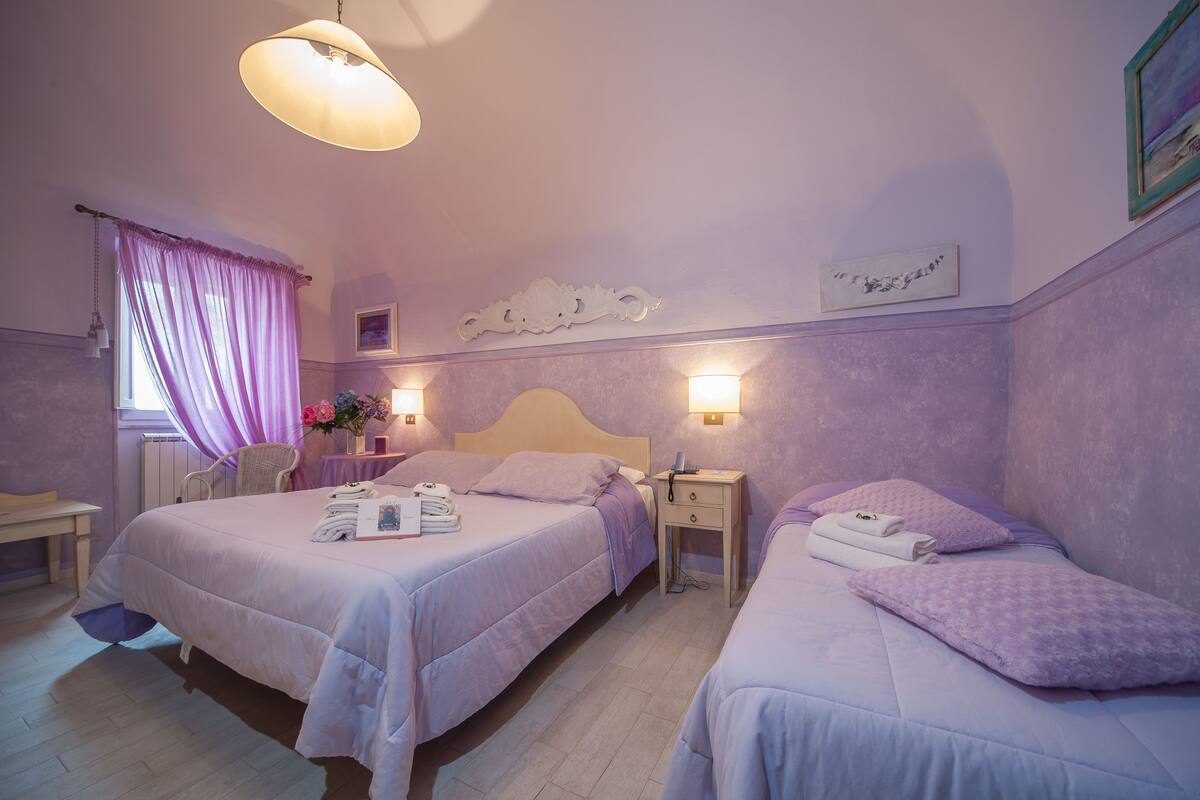 Un dormitorio con dos camas, una mesita de noche con lámpara, una silla y una ventana con cortinas.