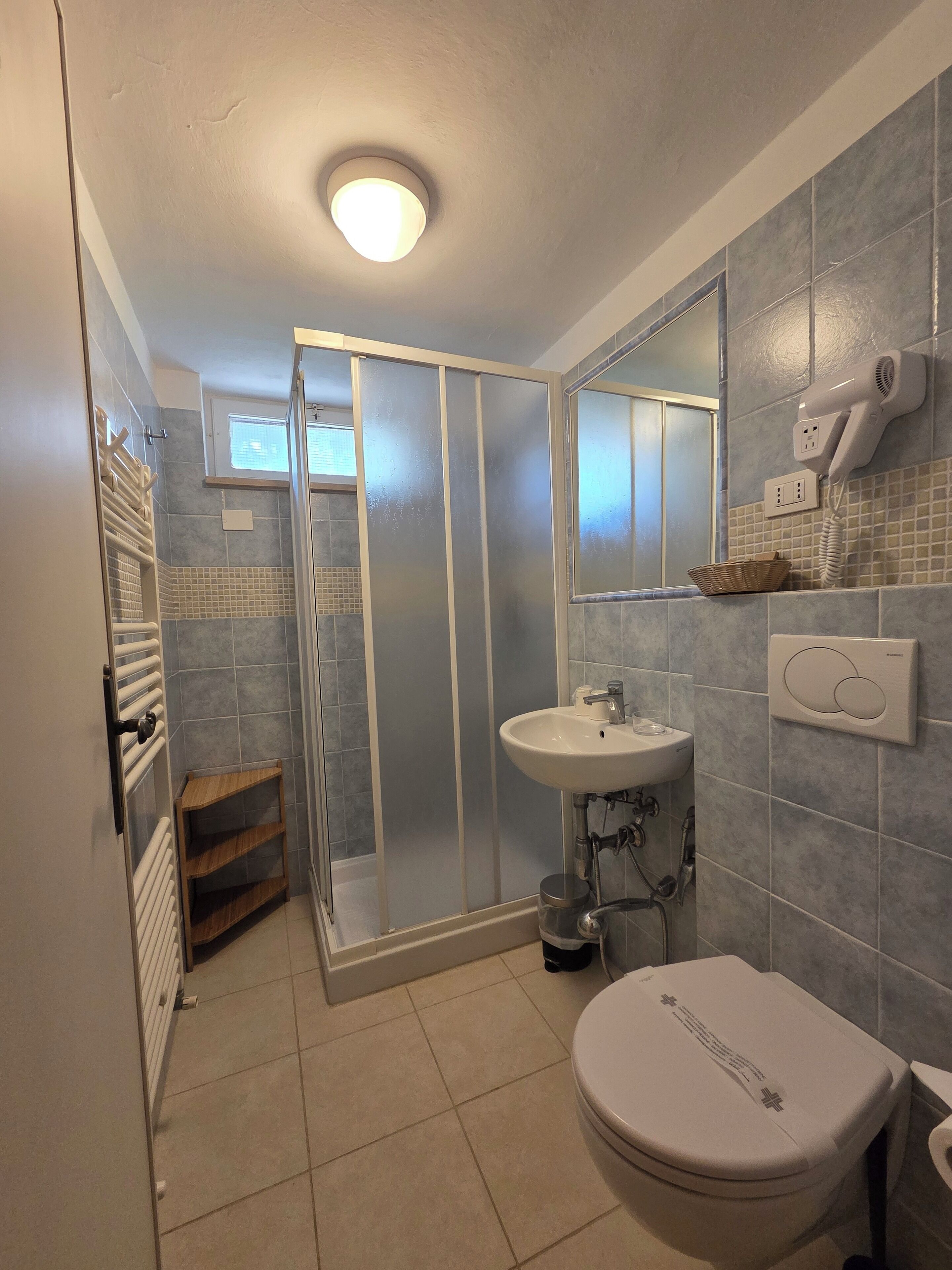 Ein Badezimmer mit Dusche, Toilette, Waschbecken und einem an der Wand befestigten Föhn.