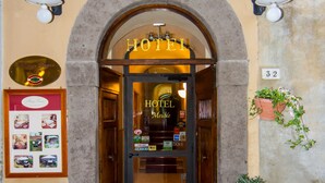 Entrada de un hotel con puerta de vidrio, felpudo y dos macetas.