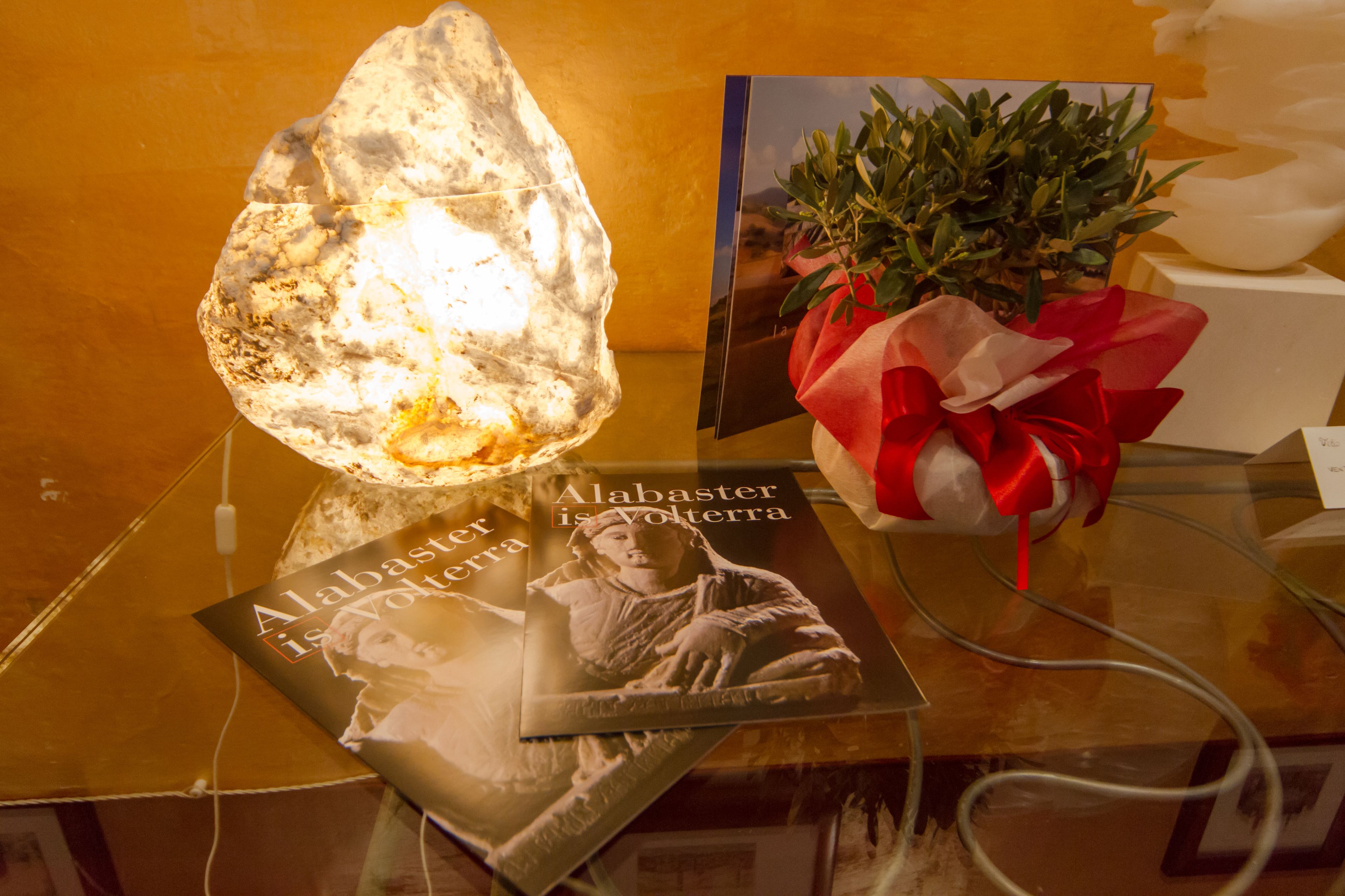 Presentatie met een boek getiteld 'Alabaster is Volterra', een decoratief gesteente en een cadeautje met een rode lint.