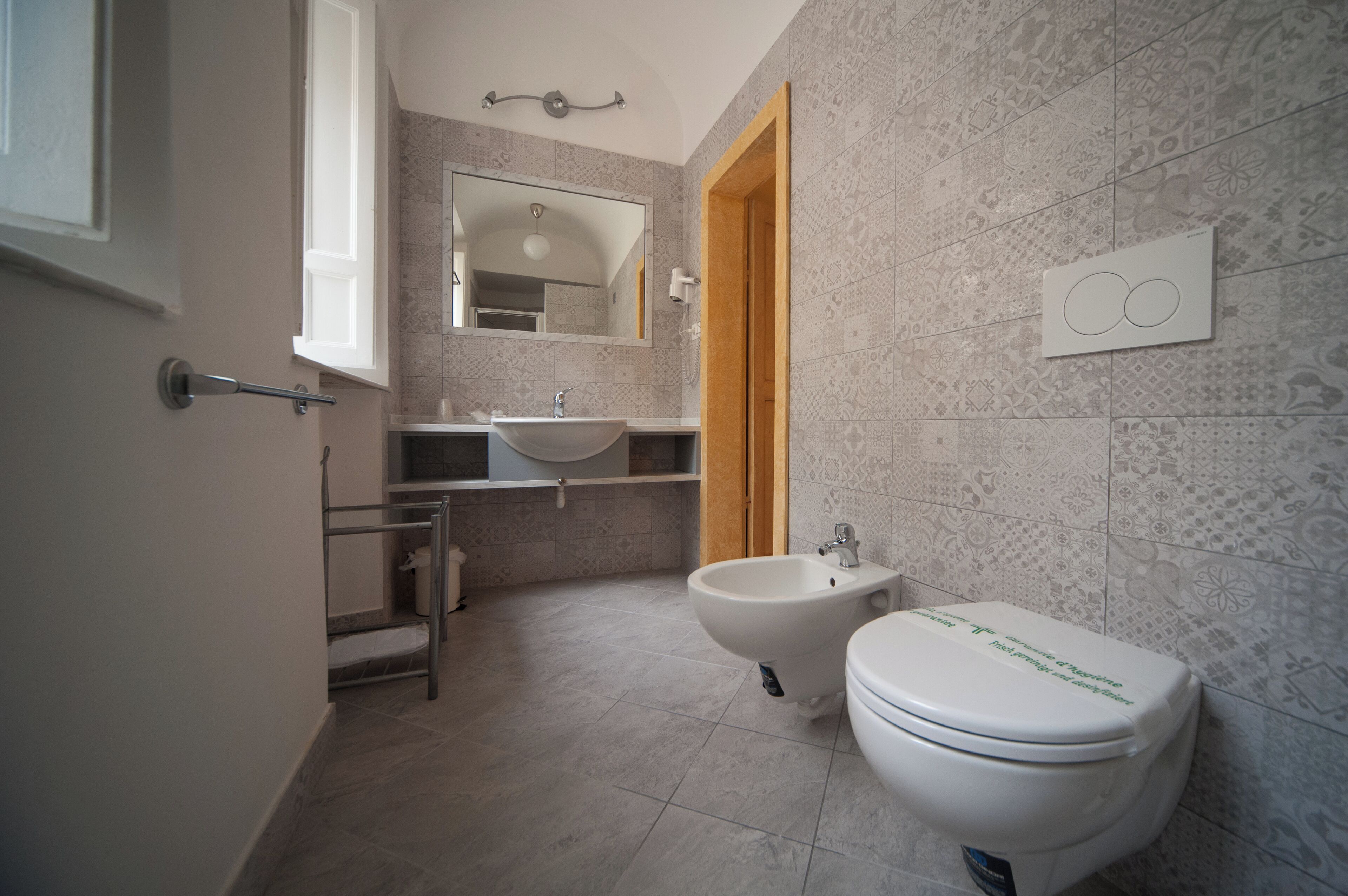 A bathroom with a bidet, toilet, sink, and mirror.