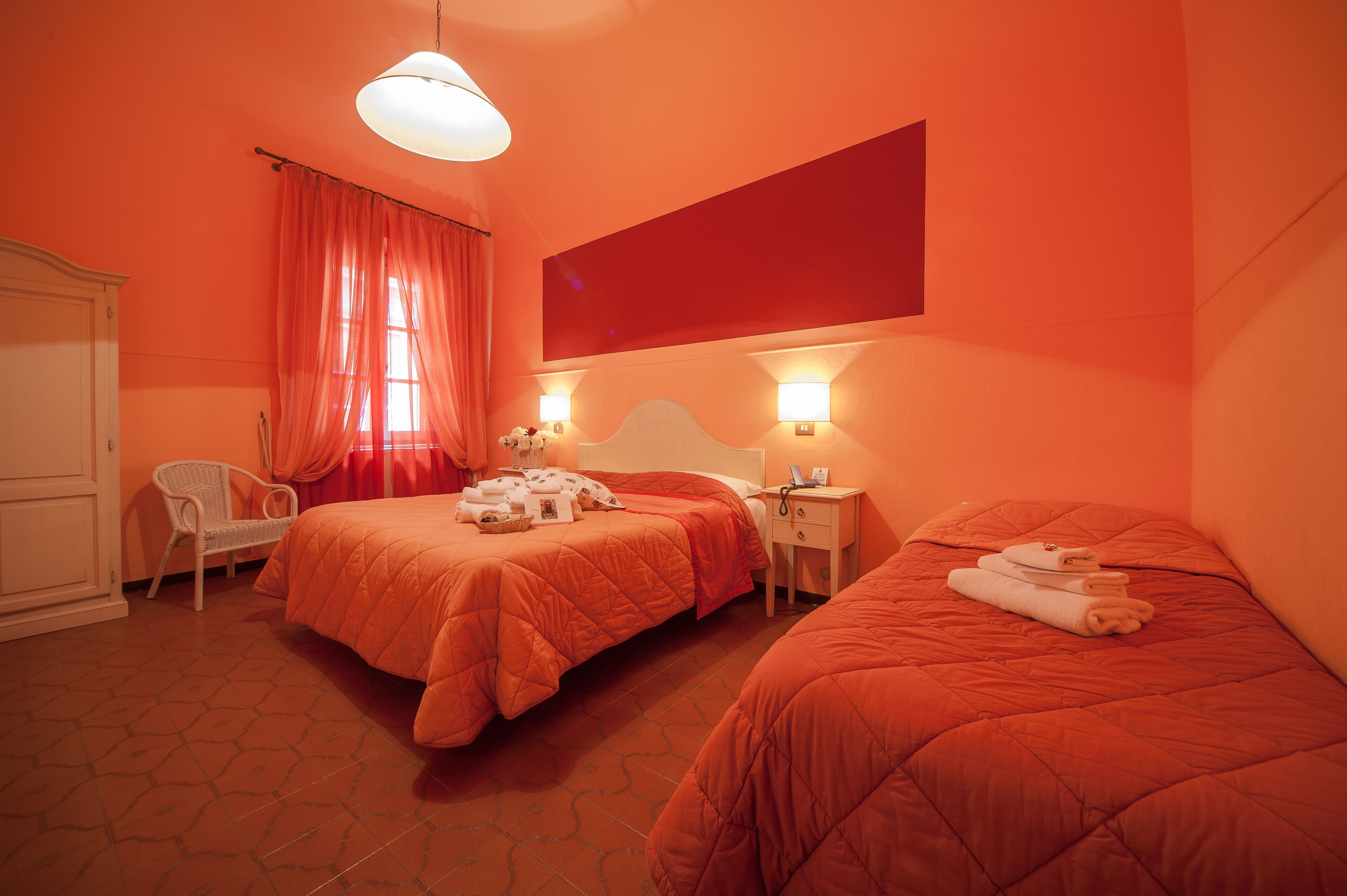 Een hotelkamer met twee bedden, een stoel, een kledingkast en een groot raam met gordijnen.