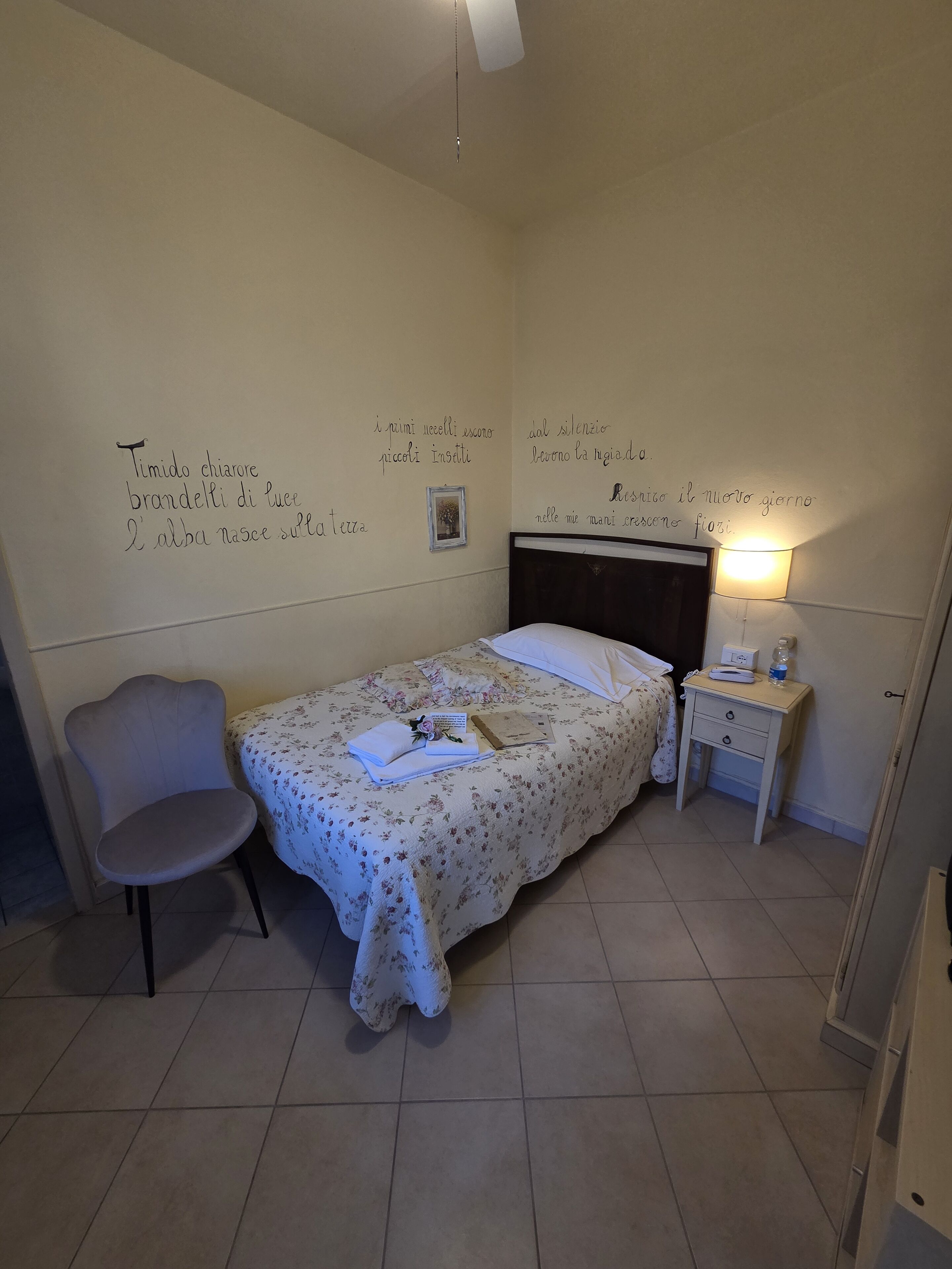 Une chambre à coucher avec un lit, une chaise, une table de chevet et une commode. On peut voir des notes manuscrites sur le mur.