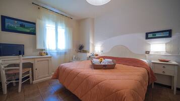 Un dormitorio con cama, escritorio, silla, mesita de noche, lámpara y un cuadro en la pared.