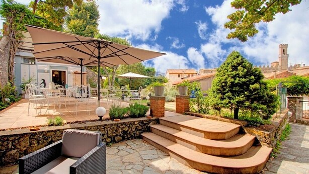 Un patio al aire libre con mobiliario de mimbre, una escalera de piedra y una vista de un edificio histórico al fondo.