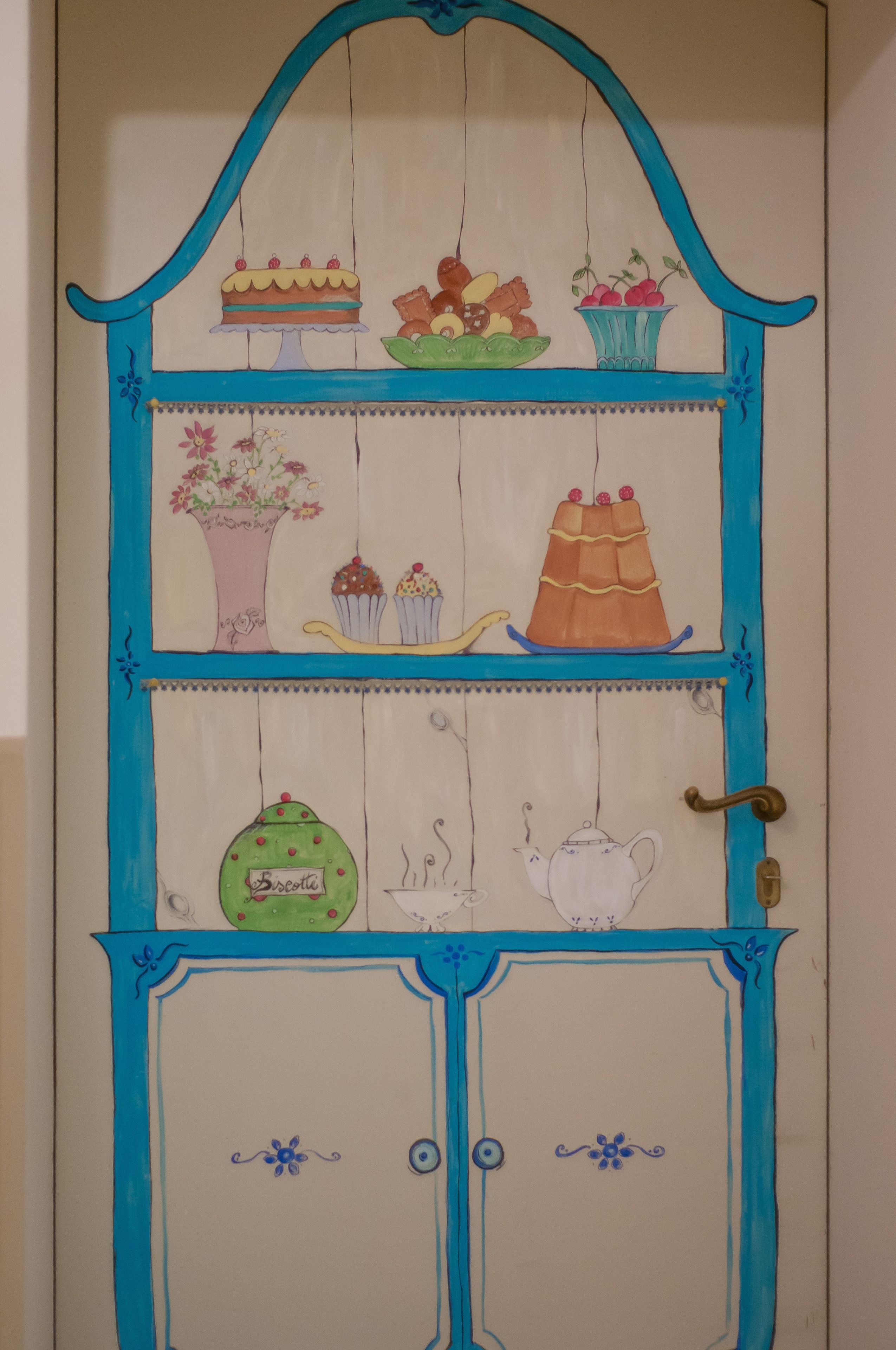 A door with a blue frame and a shelf above it displaying various items like a cake, fruits, and a vase.