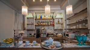 Zona de bar con estantes llenos de botellas de licores, una máquina de café y una bandeja con vajillas de té y pasteles.