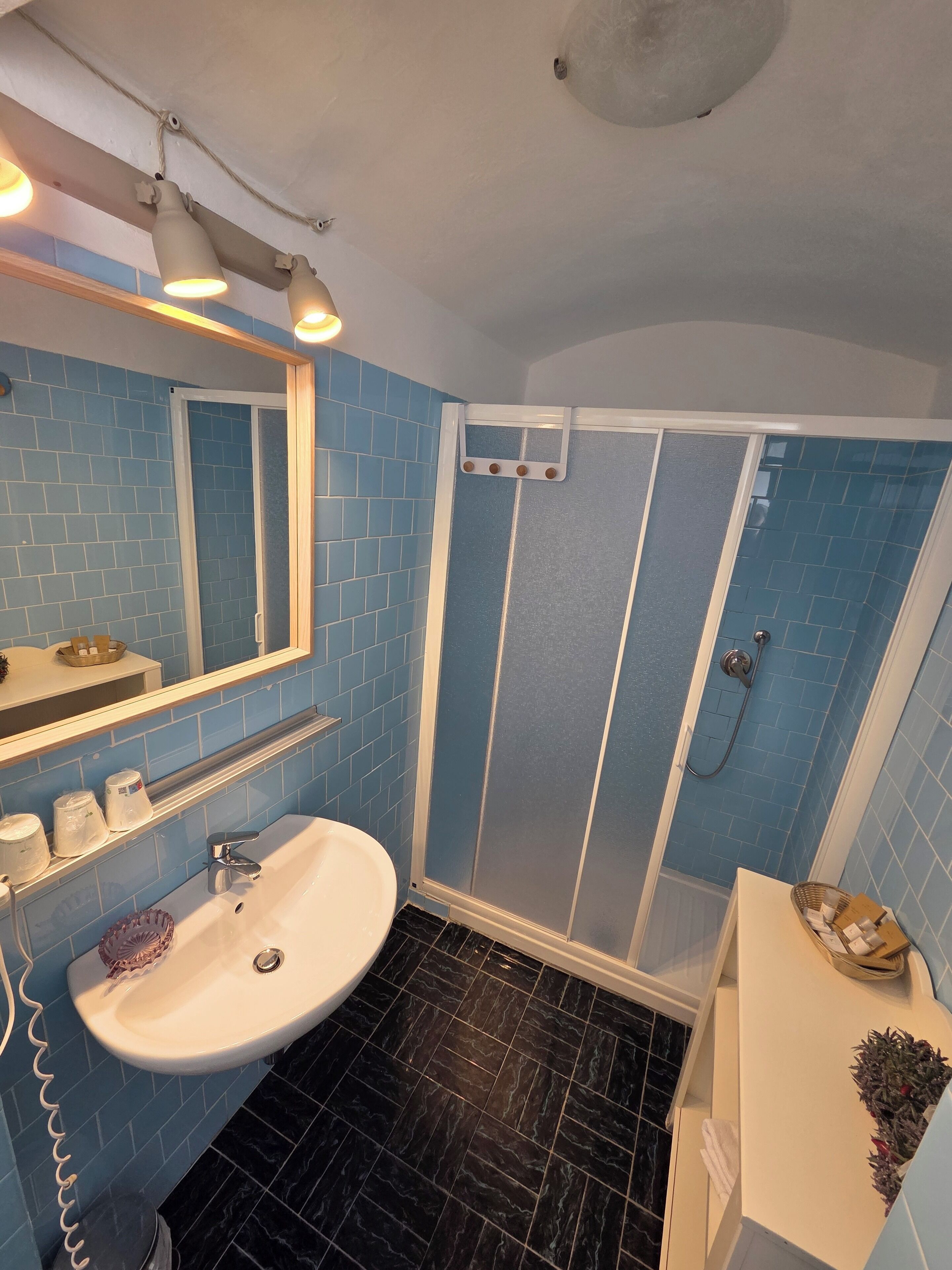 A bathroom with a white sink, blue-tiled walls, a shower enclosure, and a mirror with lights.