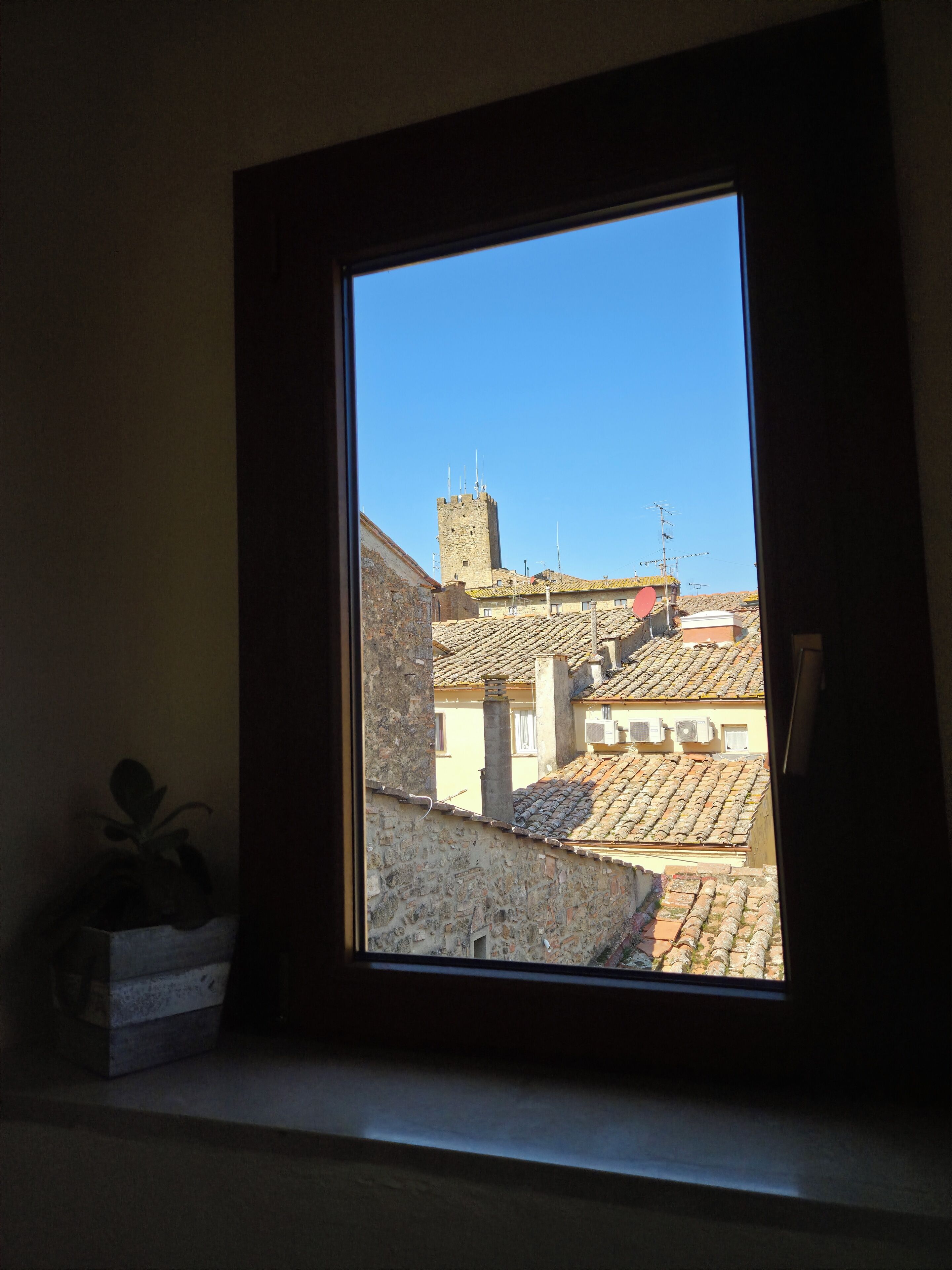 A window with a view of a building with a tower and tiled roofs.