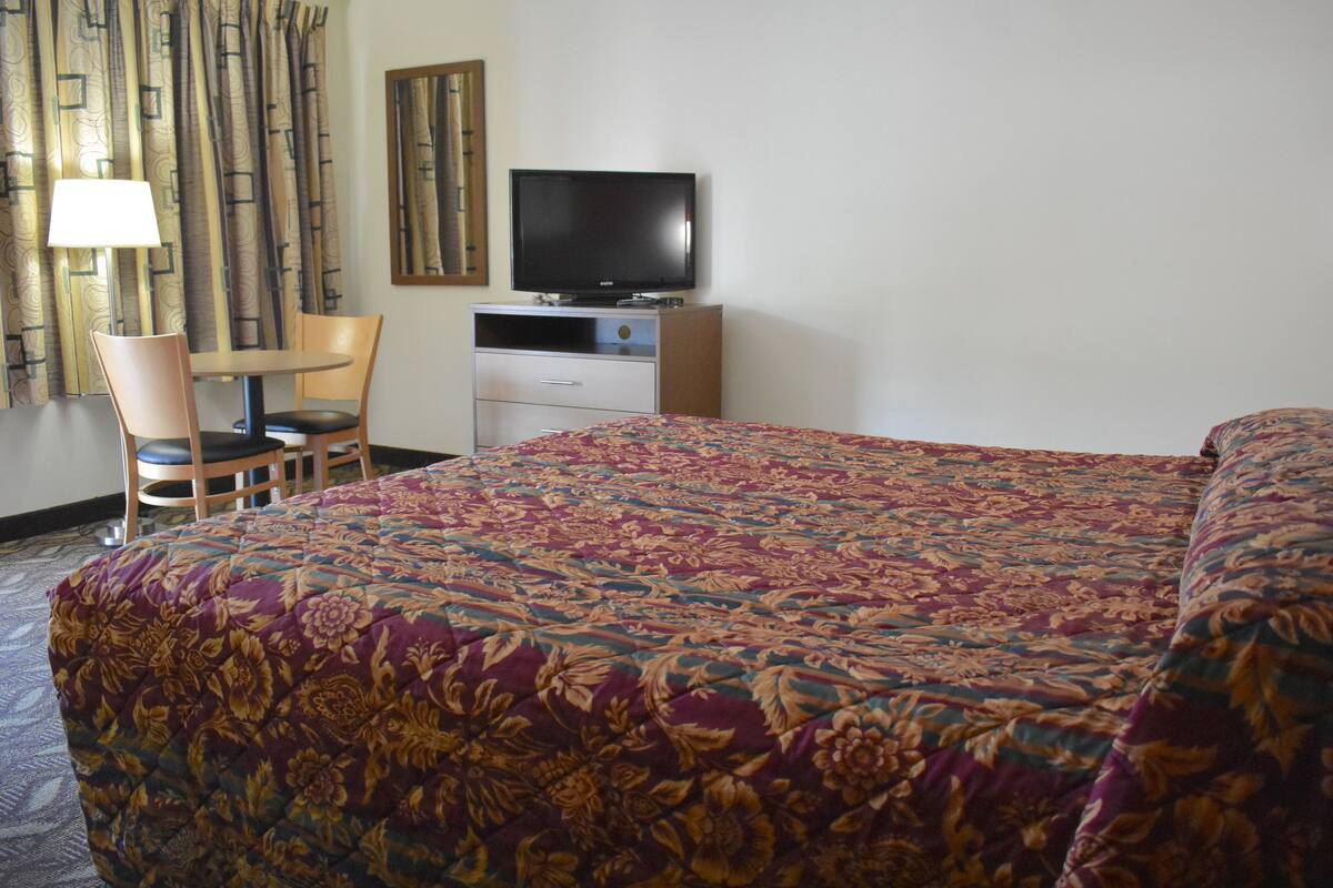 A hotel room with a large bed, a television on a dresser, a chair, and a lamp.