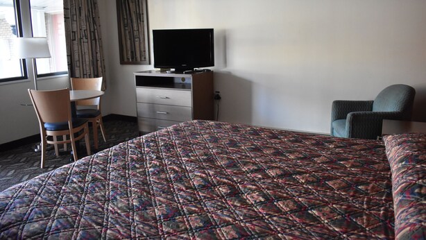 A hotel room with a large bed, a desk with a flat-screen TV, a chair, and a window with curtains. - South Hills Motel (West Mifflin)