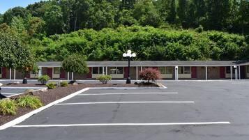 A motel with a parking lot, a small garden area, and a building with a red and beige facade.