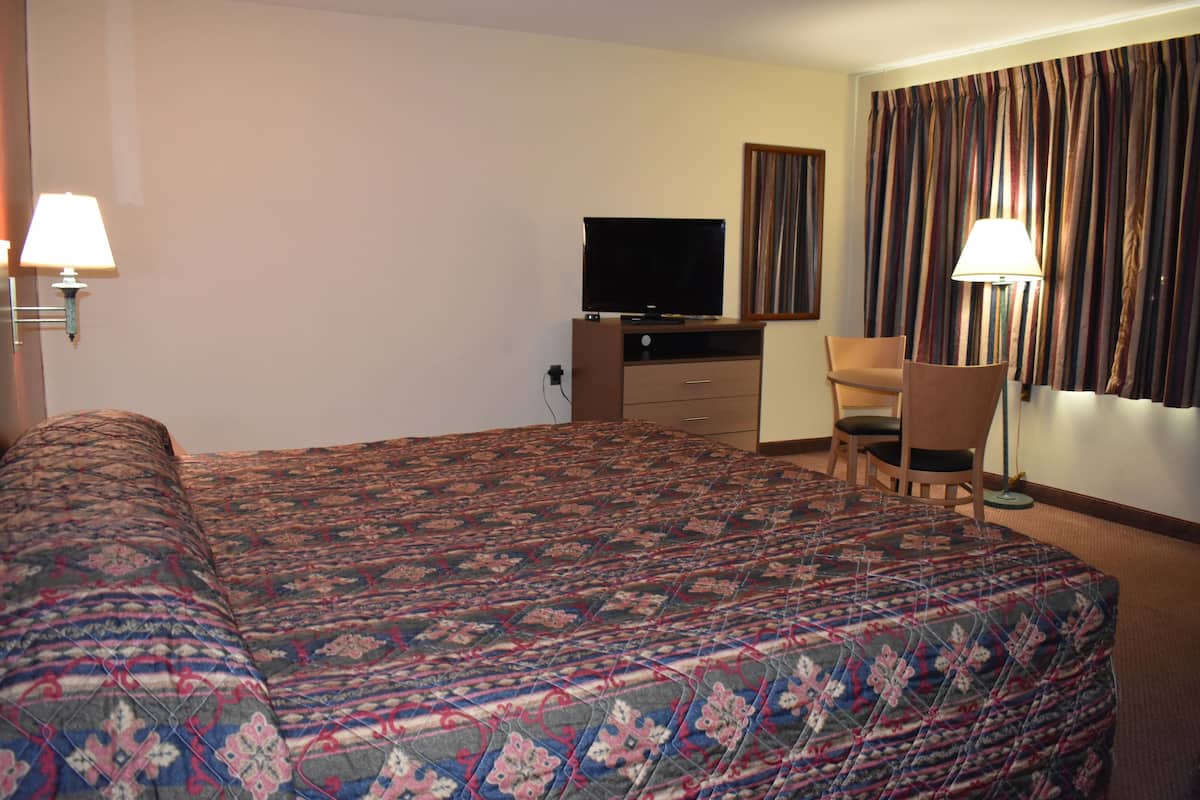 A hotel room with a large bed, a television, a desk, and a chair.